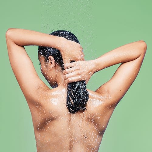 Woman, back and washing hair in studio, water and blue background for body care or wellness. Morning, bathroom routine and beauty or rinsing treatment, relaxing and hygiene grooming or cleaning
